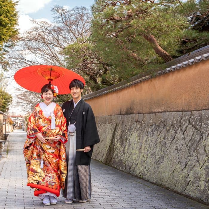 結婚写真神社で傘をさして散歩する白無垢を着た女性と羽織袴の男性新郎新婦